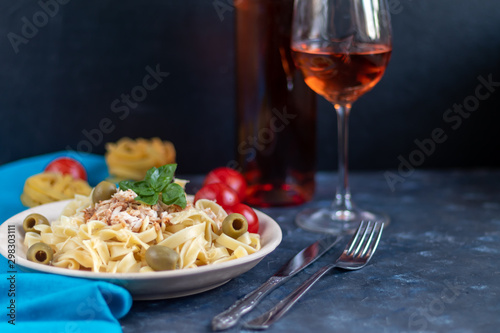 Italian pasta, spaghetti with avocado, basil, cream, cheese. Cherry tomatoes, olive oil. Meat with noodles. On a gray background. In the background is a glass of orange wine. Copy space. 