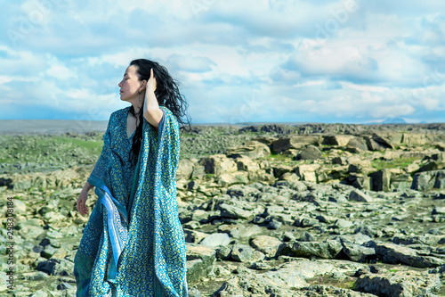 Quadro su tela Women in a blue dress fluttering in a wind standing on a lava rocks field pn wes
