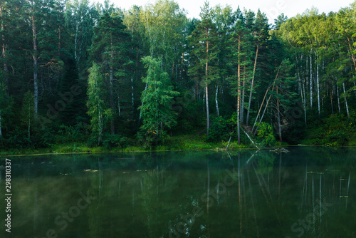 Beautiful calm lake and dark emerald forest ashore