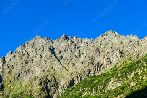 Massive, sharp stony mountain range of Schladming Alps, Austria. The mountain has a pyramid shape, it is partially overgrown with green bushes. Dangerous mountain climbing.Clear and beautiful day. photo