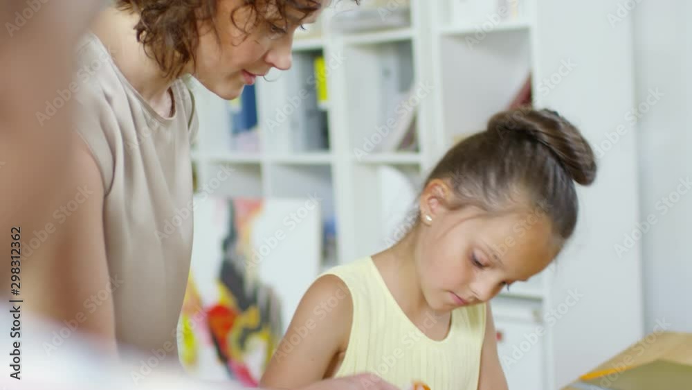 Female teacher making paper craft with little caucasian and african girl during educational game in kindergarten Female teacher making paper craft with little caucasian and african girl during educational game in kindergarten