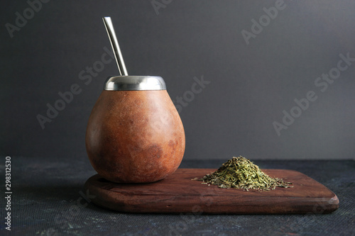 Obraz na płótnie Calabas and a bombilla with a bunch of mate tea on a wooden plate on dark background