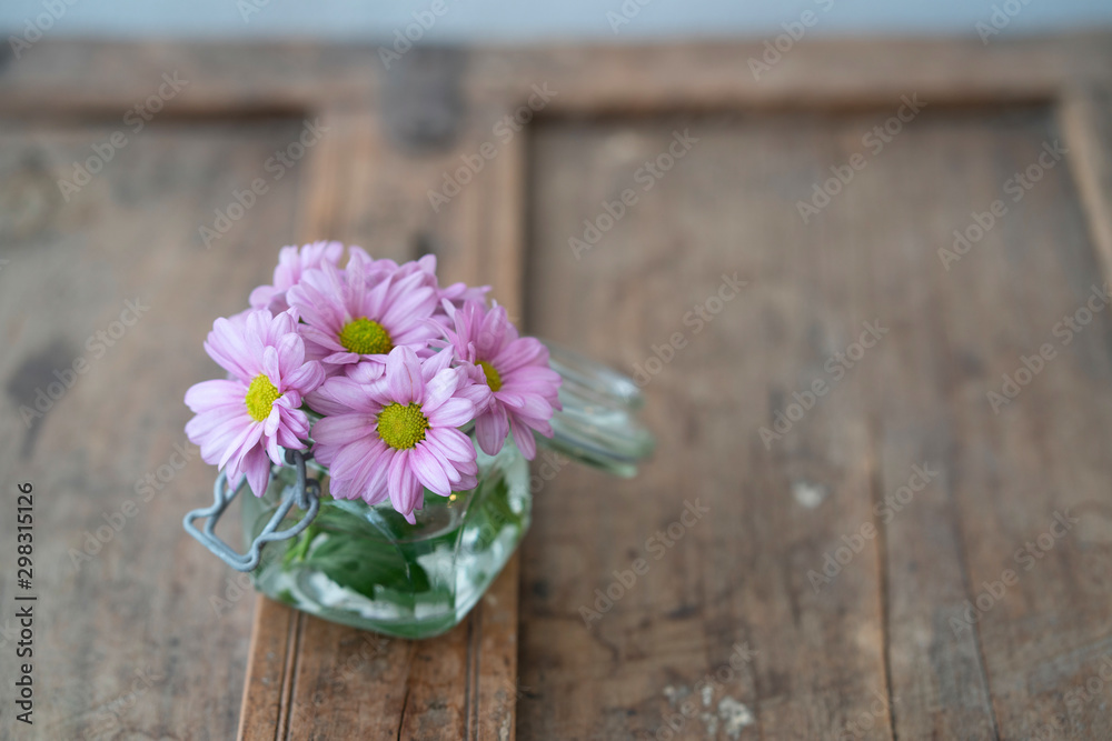 Small bouquet of summer flowers in glass on shabby used wooden furniture