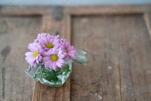 Small bouquet of summer flowers in glass on shabby used wooden furniture