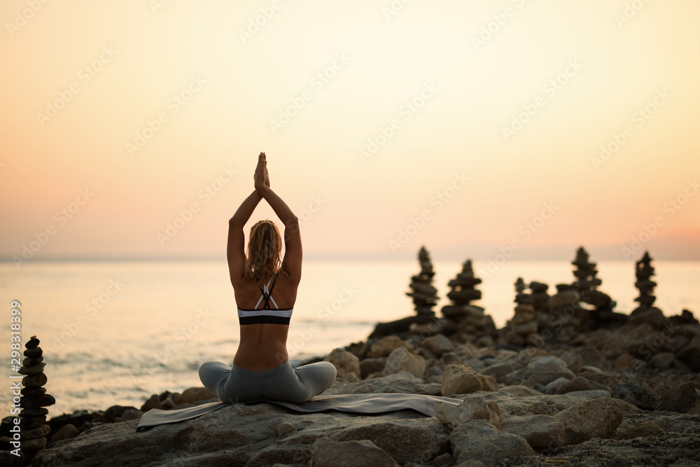 Back view of woman with hands above head meditating at sunset.
