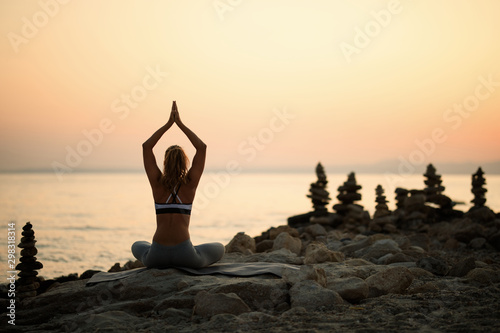 Rear view of woman practicing Yoga on the beach at sunset.
