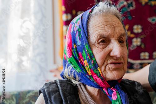 old woman with wrinkled skin face, hands sitting alone in house.
