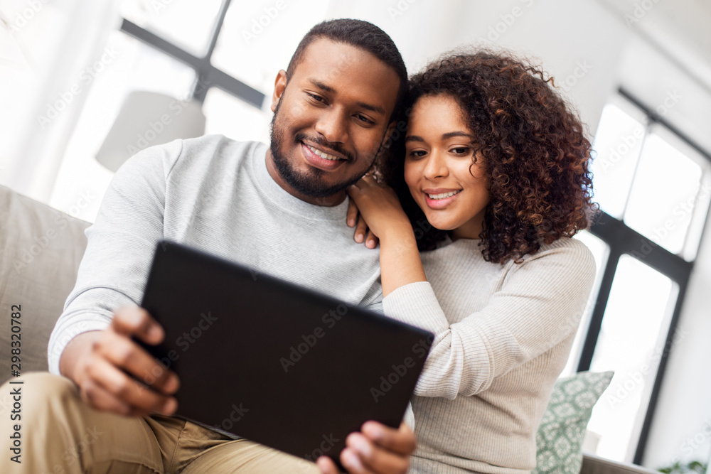 Obraz premium technology, internet and people concept - happy african american couple with tablet computer at home