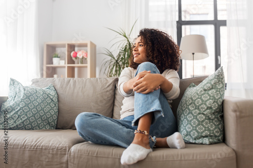 people, race, ethnicity and portrait concept - happy african american young woman sitting on sofa at home photo