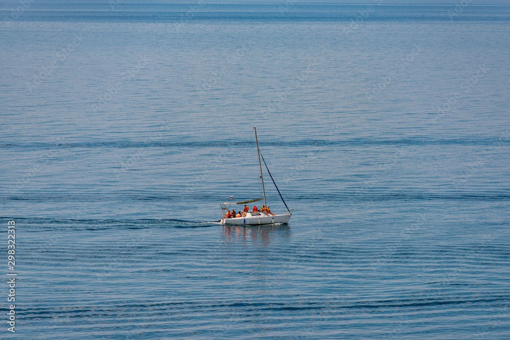 Aerial view on a white floating sailboat with people in it in the blue black sea