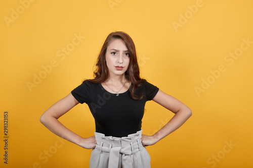 Cute girl standing in front of orange background not happy for sure. She is in shock as someone did something she never expected which has risen many questions in her mind.