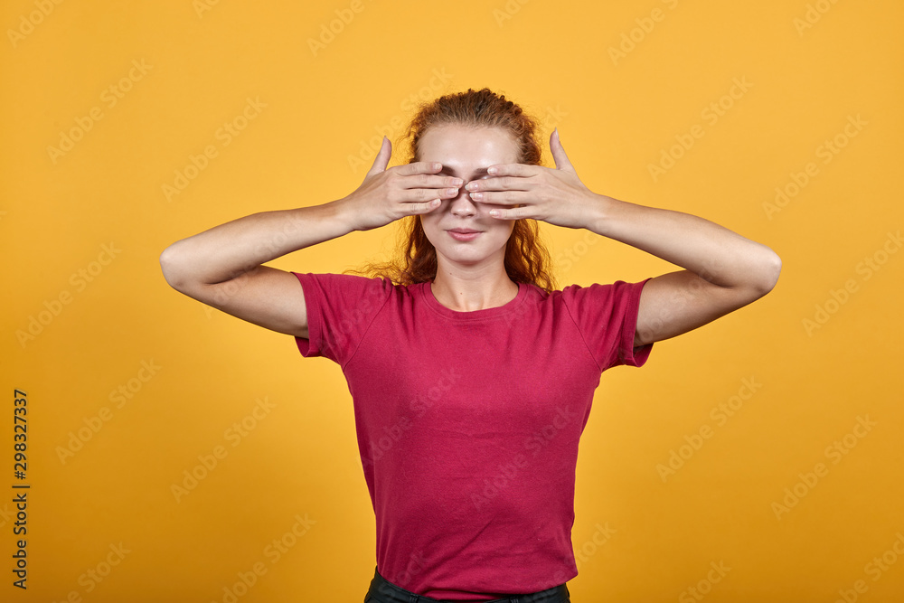 Gorgeous European woman closing eyes with her both hands. Pretty girl with dark hair in beautiful outfit has professional photosession over isolated yellow background. Gorgeous European woman closing eyes with her both hands. Pretty girl with dark hair in beautiful outfit has professional photosession over isolated yellow background.
