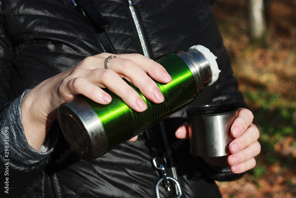 Naklejka premium Woman pours tea from a thermos in the woods