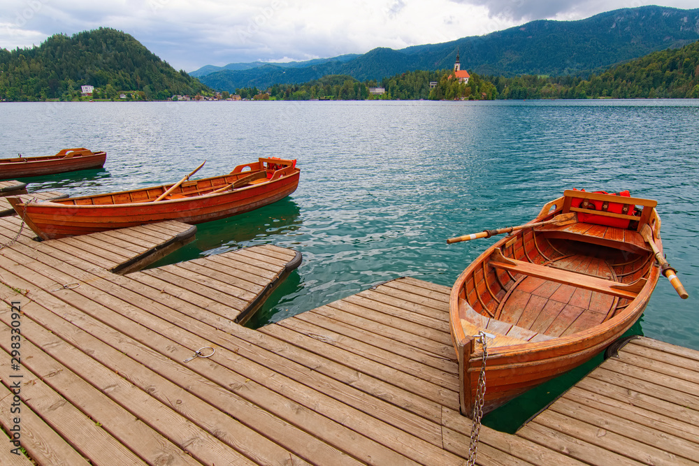 Scenic nature landscape with wooden pier and moored boats on Bled Lake (Blejsko jezero). Famous touristic place and travel destination in Europe. Bled, Slovenia
