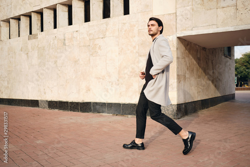 Obraz na plátně Young handsome stylish man in coat confidently walking outdoor