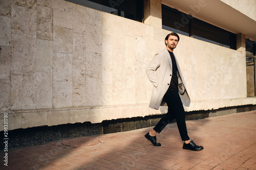 Young handsome man in coat thoughtfully looking away on street