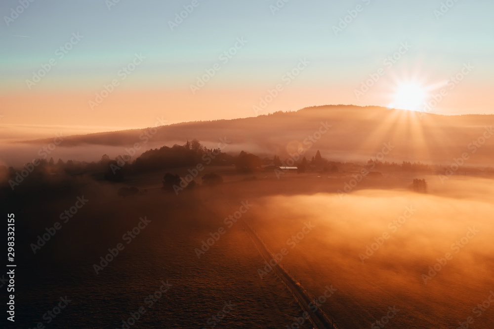 Aerial view to misty orange fog with path and hill at sunrise, Czech landscape
