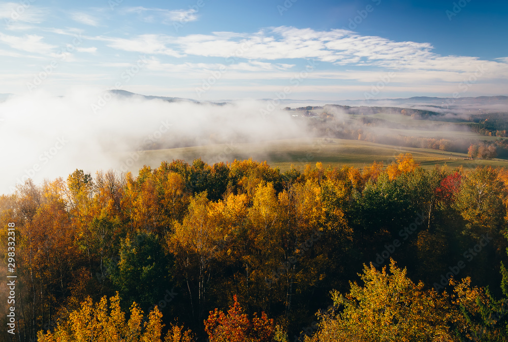 Aerial view to autumn foliage trees with misty fog and hill in sunrise, Czech landscape, colored photo