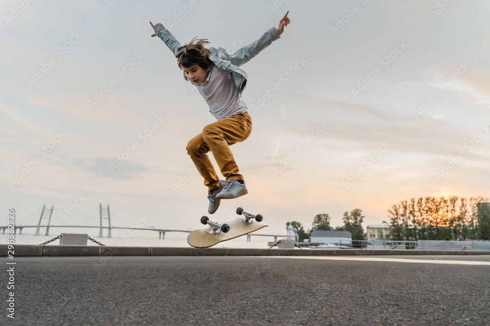 Boy jumping on skateboard at the street. Funny kid skater practicing ollie  on skateboard at sunset. Stock Photo