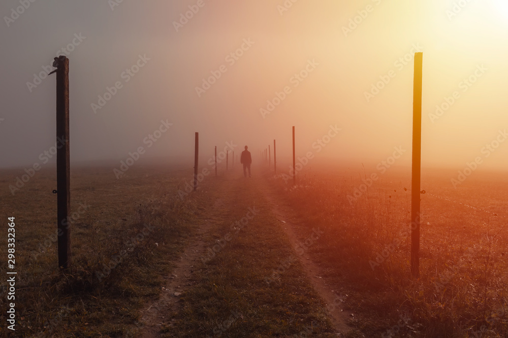 Silhouette young man walk on path with wooden stick in misty fog at sunrise, Czech landscape