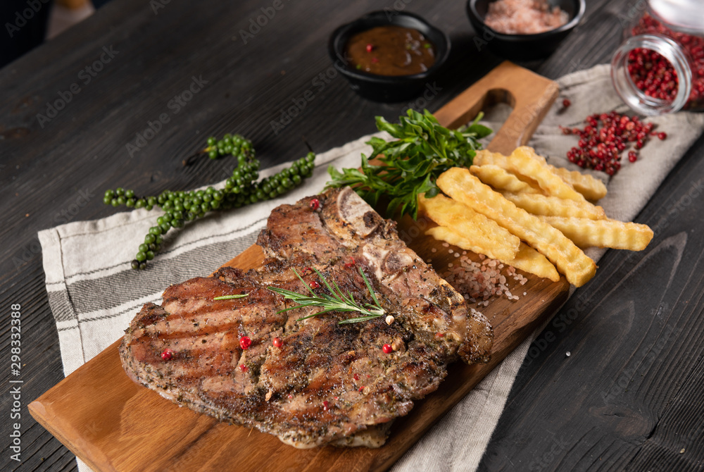 The steak of beef grilled served with french frie placed on chop real wood, no dish and decorate with many herb as pepper and rosemary. All placed on the grey dish towel and wood background. Flat lay The steak of beef grilled served with french frie placed on chop real wood, no dish and decorate with many herb as pepper and rosemary. All placed on the grey dish towel and wood background. Flat lay