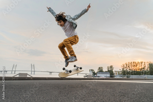 Boy jumping on skateboard at the street. Funny kid skater practicing ollie on skateboard at sunset. photo