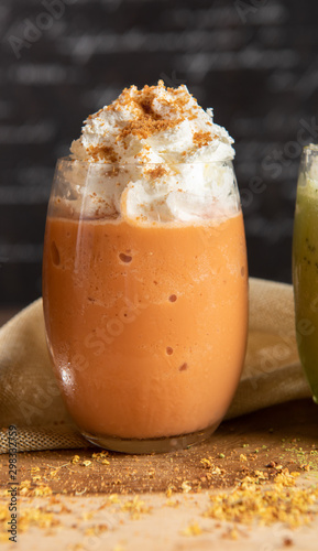 Fotografia Thai tea smoothie, decorate topping with whipping cream in a clear glass on a chopper with dark gray real wood floor