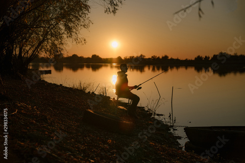 Silhouette of a fisherman. A man catches a fish by the river at sunset.