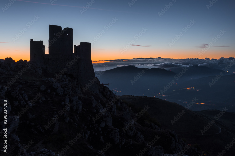 Silhouette of ruins of medieval castle of Rocca Calascio at sunrise with mountains and foggy landscape in background , Abruzzo, Italy