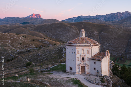 Beautiful chapel Chiesa di Santa Maria della Pietà at sunrise with barren landscape and alpine glowing mountain of Corno Grande in background, Rocca Calascio, Abruzzo, Italy