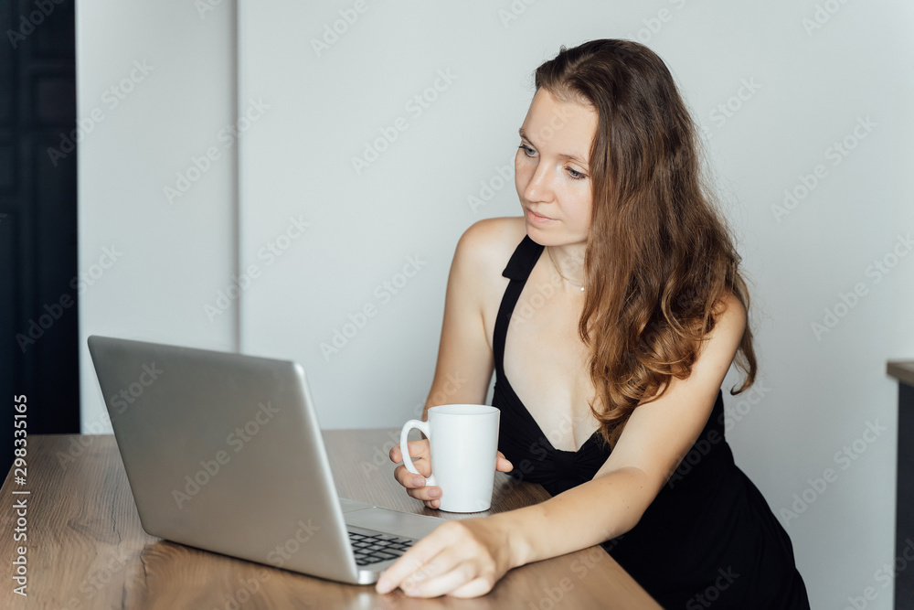 Young beautiful sad girl sits at a table in front of a laptop and dreams. Freelance, remote work Young beautiful sad girl sits at a table in front of a laptop and dreams. Freelance, remote work
