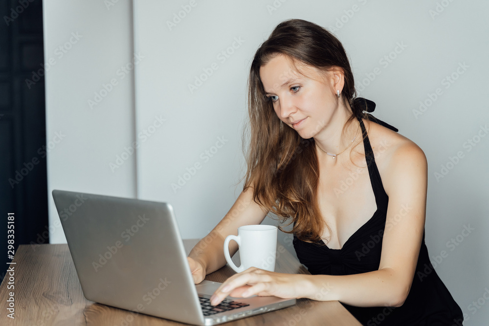 Young beautiful sad girl sits at a table in front of a laptop and dreams. Freelance, remote work Young beautiful sad girl sits at a table in front of a laptop and dreams. Freelance, remote work