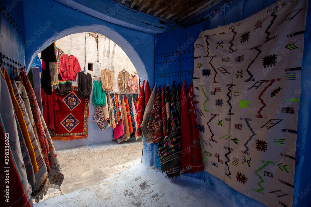 Obraz premium Narrow streets and blue painted houses of Chefchaouen city, Morocco. Most of the streets full of handmade colorful crafts,carpets and souvenir hanged to the walls of the blue houses.