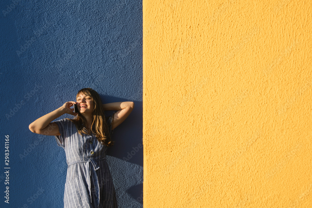 Happy woman on the phone in front of yellow and blue walls