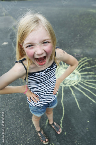 Germany, North Rhine Westphalia, Cologne, Portrait of girl drawing sun on street, smile, close up photo