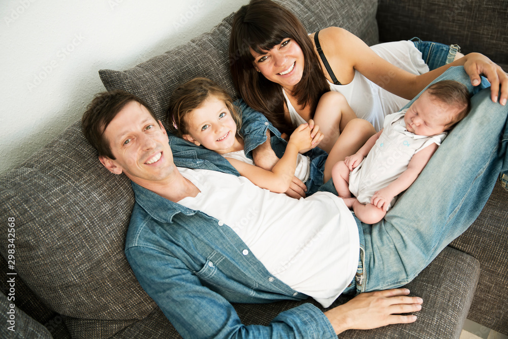 Young parents with male newborn and little daughter sitting on sofa at home Young parents with male newborn and little daughter sitting on sofa at home