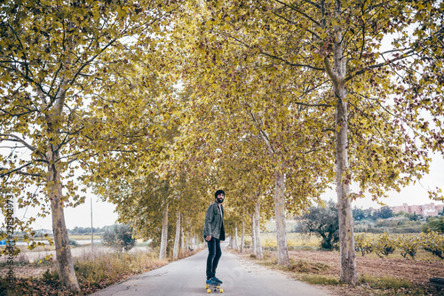 Spain, Tarragona, young man with longboard on autumnal country road photo