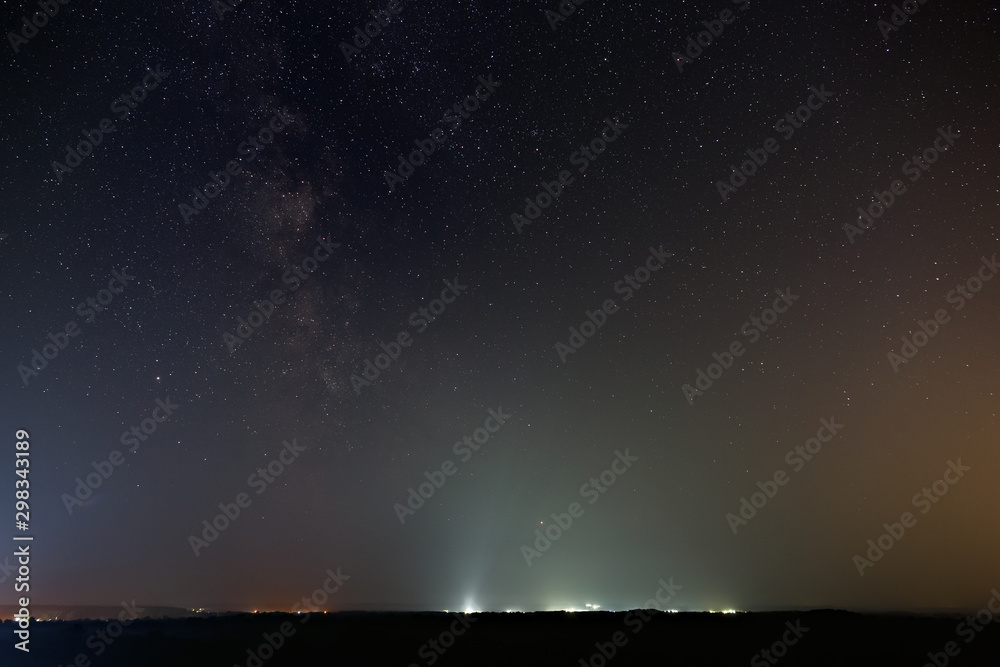 Stars of the milky way galaxy in the night sky. The horizon is illuminated by the light of the city.