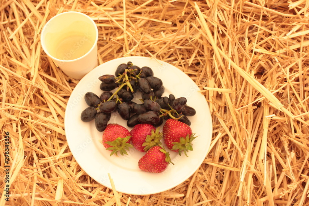 Fresh delicious and healthy fruits and berries called grapes and strawberries in a white plate.  Country style breakfast on the grass