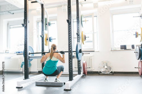 Woman doing barbell squats in a power rack photo