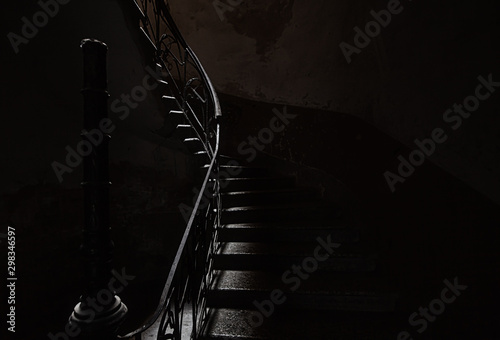 Obraz na płótnie An ancient screw staircase in a dark entrance, a small ray of light illuminates the steps