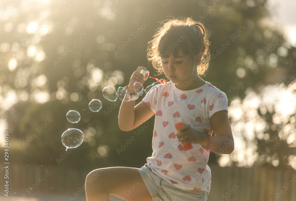 Little girl making soap bubbles in the park at twilight Little girl making soap bubbles in the park at twilight