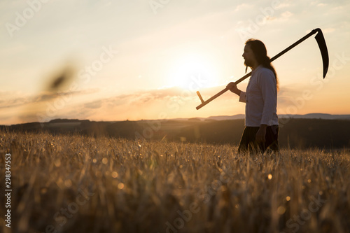 Organic farmer with scythe in barley field at sunrise photo