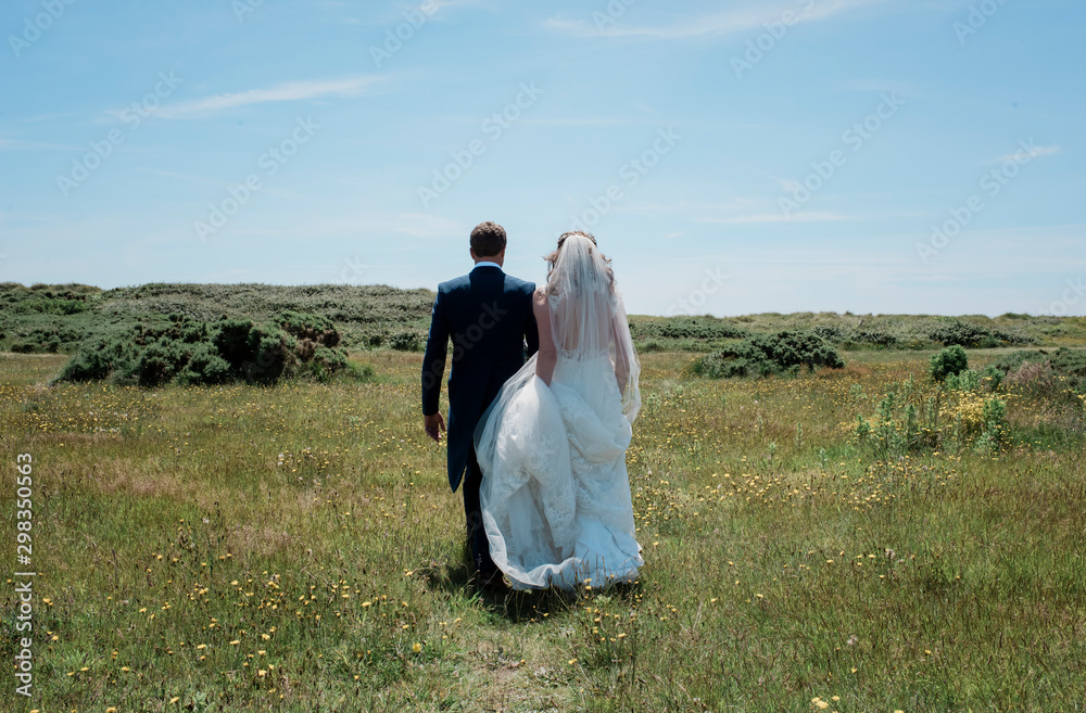 Bride and groom walking through a field of green on their wedding day Bride and groom walking through a field of green on their wedding day