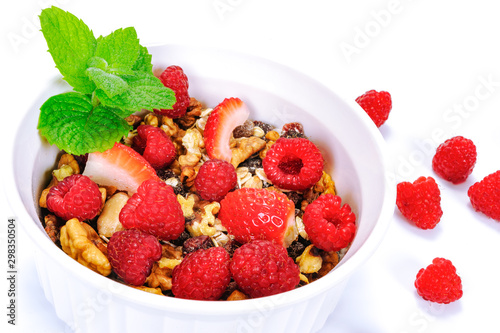 Bowl of homemade organic granola with oats  nuts  raspberries and strawberries decorated with leaves of mint in close-up