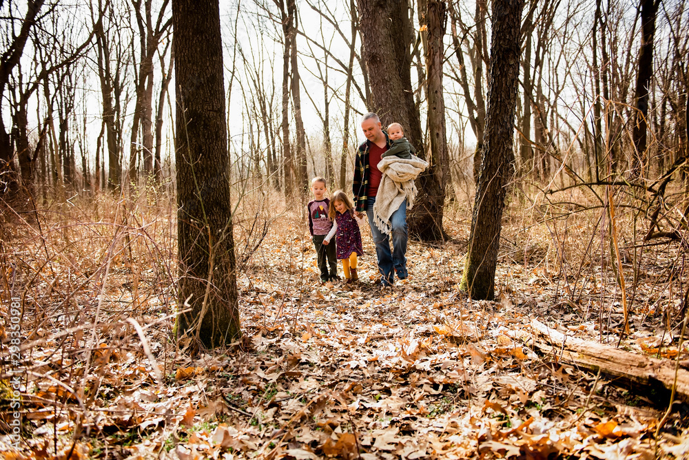 Father walks in woods with children holding baby and daughters hand Father walks in woods with children holding baby and daughters hand