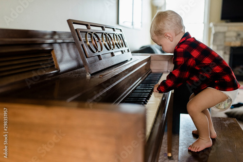 Baby boy in diaper stands on bench playing piano at home photo