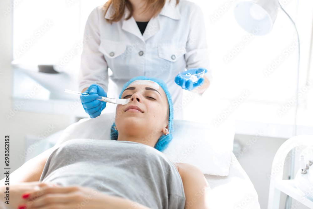 Naklejka premium Woman professional doctor beautician applies a mask on a patient's face for skin care. Cosmetic procedures for skin rejuvenation and nutrition