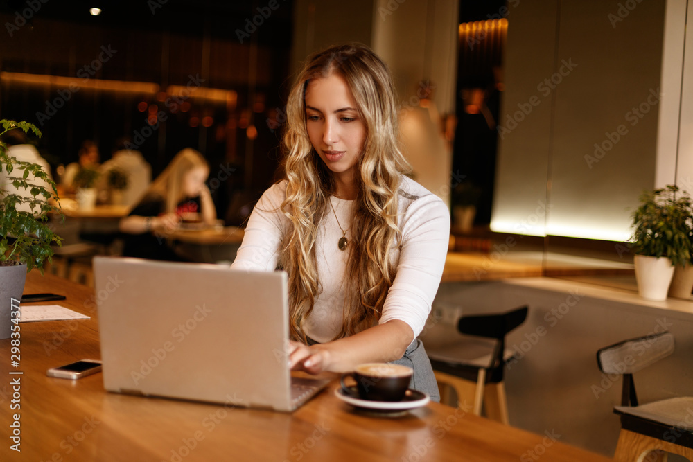 Technology. Work. Freelance. Young woman is working with her laptop and smiling while sitting in cafe Technology. Work. Freelance. Young woman is working with her laptop and smiling while sitting in cafe