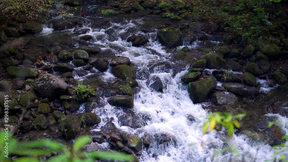 Slow motion of cold fresh water in natural waterfall located in dark moody forest around boulders and rocks with shallow depth of field Slow motion of cold fresh water in natural waterfall located in dark moody forest around boulders and rocks with shallow depth of field